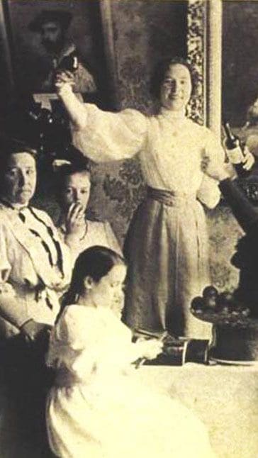 A woman standing with four girls in white dresses among framed portraits in the Stember studio