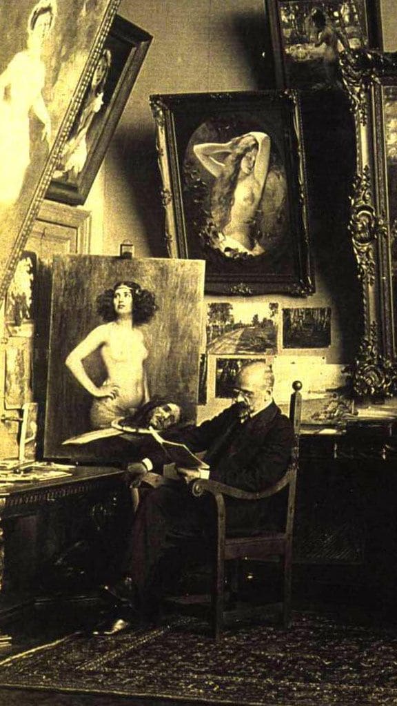 Victor Stember seated at his writing desk, landscape studies pinned to the wall and a painting of a standing nude behind him