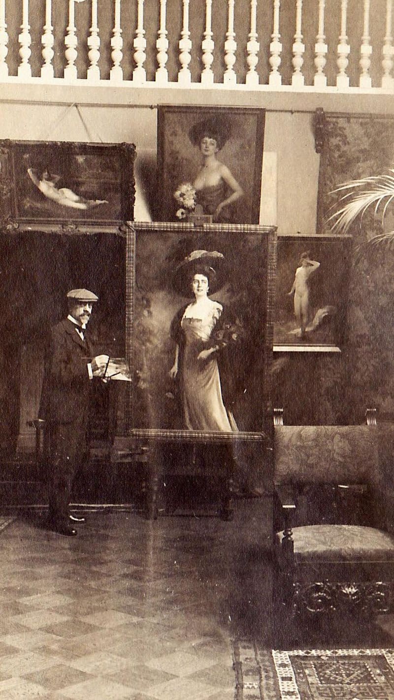 A wall of framed Stember portraits arranged against draped cloth in an exhibition hall, with a potted laurel tree between them